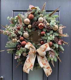 a christmas wreath with pine cones and ornaments hanging on the front door, ready to be hung