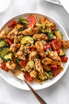 a white bowl filled with chicken and veggies on top of a marble table