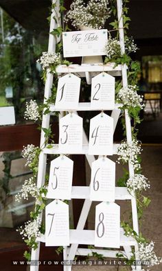 a white ladder decorated with greenery and seating cards for an outdoor wedding or reception