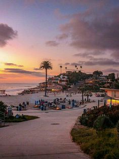 people are walking on the beach at sunset with palm trees and buildings in the background