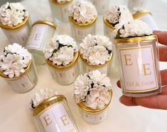 a hand holding a can filled with flowers on top of a white table covered in gold trim