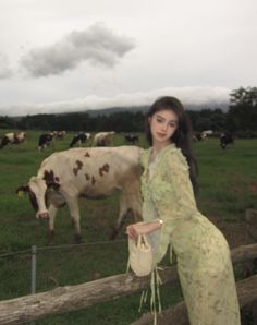 a woman standing next to a fence with cows in the background