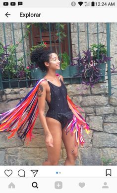 a woman in a bathing suit with colorful streamers on her head and arms, standing next to a stone wall