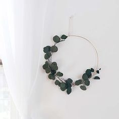 a wreath made out of green leaves on a white wall with curtains in the background