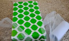 a green and white paper bag sitting on top of a floor next to a pair of scissors