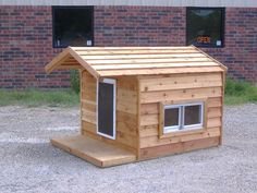 a small wooden dog house sitting on top of a gravel field next to a brick building