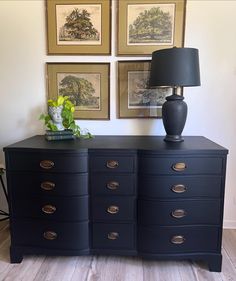 a black dresser with two lamps and pictures on the wall