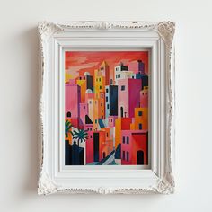 a painting on the wall of a white frame with an orange and pink cityscape