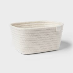 a white woven basket with handles on the front and bottom, sitting on a grey surface