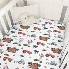 a white crib with a red and green tractor print on the bed sheet that is next to a stuffed animal