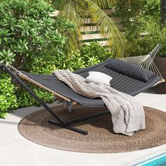 a hammock is sitting next to a pool with a blanket and pillows on it