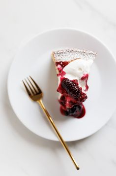 a white plate topped with a slice of cake and covered in berries next to a fork