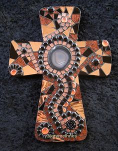 a cross made out of mosaic tiles on a black surface with the center surrounded by beads