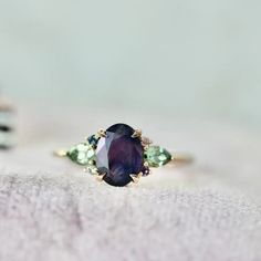 a close up of a ring with an oval shaped purple stone surrounded by green and blue stones