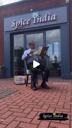 a man sitting in a chair reading a newspaper outside a store front with the words spice india on it