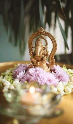 a small gold statue sitting on top of a table next to flowers and a lit candle