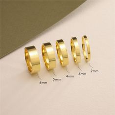 four different sizes of gold wedding rings on a white surface with measurements for each ring