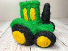 a green and black toy tractor sitting on top of a wooden table next to a white wall