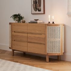 a wooden dresser with two candles on top of it next to a painting and rug