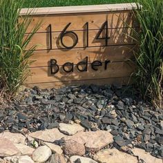 a wooden sign sitting on top of a pile of rocks in front of some grass