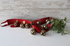 a red ribbon with bells on it next to a pine branch and some white flowers