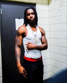 a man standing in front of a locker with his arms crossed and wearing a white tank top