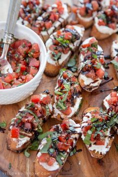 a wooden cutting board topped with slices of bread covered in toppings