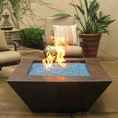 a fire pit sitting on top of a patio next to a chair and potted plant