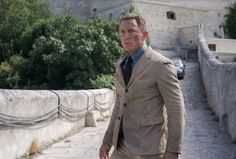 a man in a suit and tie walking down a street next to a stone bridge