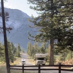 two rvs are parked on the side of the road in front of some trees