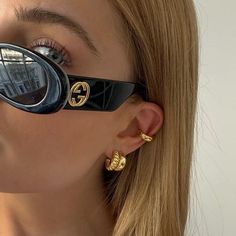 a woman with sunglasses on her face wearing gold earring and black eyeglasses