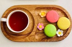 a cup of tea and some cookies on a wooden platter with pink, yellow, and green frosting