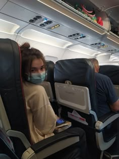 a woman wearing a face mask while sitting on an airplane with another man in the background