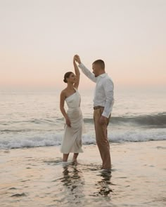 a man and woman are standing in the water at the beach holding each other's hands