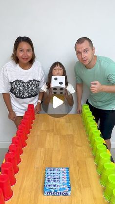 three people standing around a wooden table with cups on it and one person holding up a camera