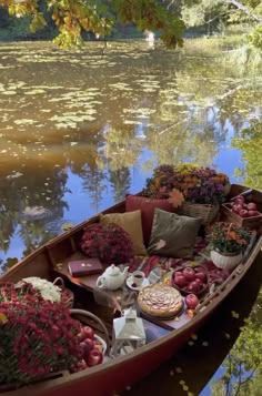 a boat filled with lots of flowers sitting on top of a river next to a forest