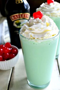 two cups filled with whipped cream and cherries next to a bottle of bailey's