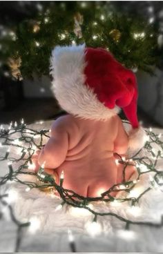 a baby wearing a santa hat sitting in front of a christmas tree