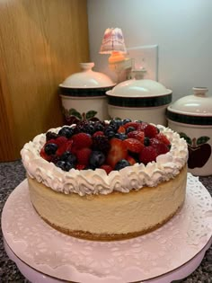 a cake with berries and whipped cream on top sits on a plate in front of other cakes