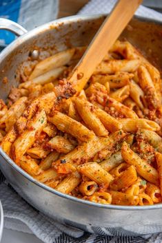 a pan filled with pasta and sauce on top of a cloth next to a wooden spoon