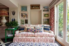 a living room filled with furniture next to a window covered in curtains and paintings on the wall