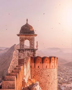 an old stone building on top of a hill with birds flying around it and in the background