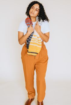 a woman in white shirt and orange pants holding a yellow purse with black stripes on it