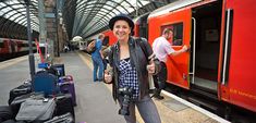 a woman standing in front of a red train at a train station with lots of luggage