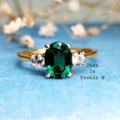 a green ring sitting on top of a blue surface next to white and gold flowers