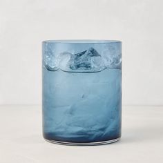 a blue glass filled with ice on top of a white table next to a wall