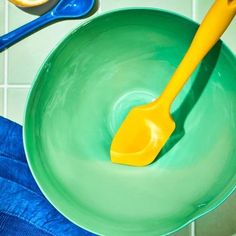 a yellow spoon sitting in a green bowl on top of a blue towel next to orange slices