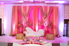 a couch sitting on top of a white table covered in pink and gold cloths