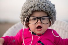 a small child wearing glasses and a knitted hat with pearls on it's head