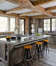 a large kitchen with wooden floors and an island in the middle, surrounded by three yellow stools